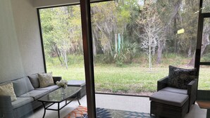 A modern living room with a large sliding glass door, a grey sofa, a chair, and a patterned rug. - Beautiful 4-bedroom house with AC in Ormond Beach (Ormond Beach)