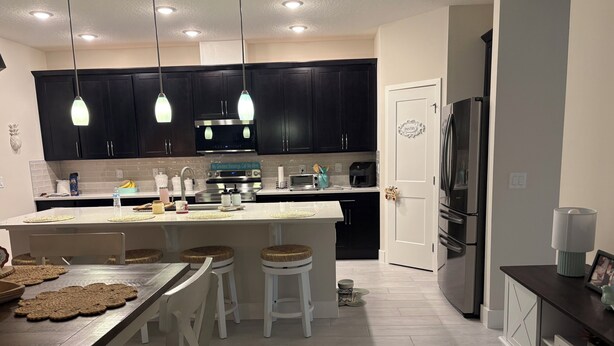 A modern kitchen with dark cabinets, a central island with stools, a refrigerator, and a microwave. - Beautiful 4-bedroom house with AC in Ormond Beach (Ormond Beach)