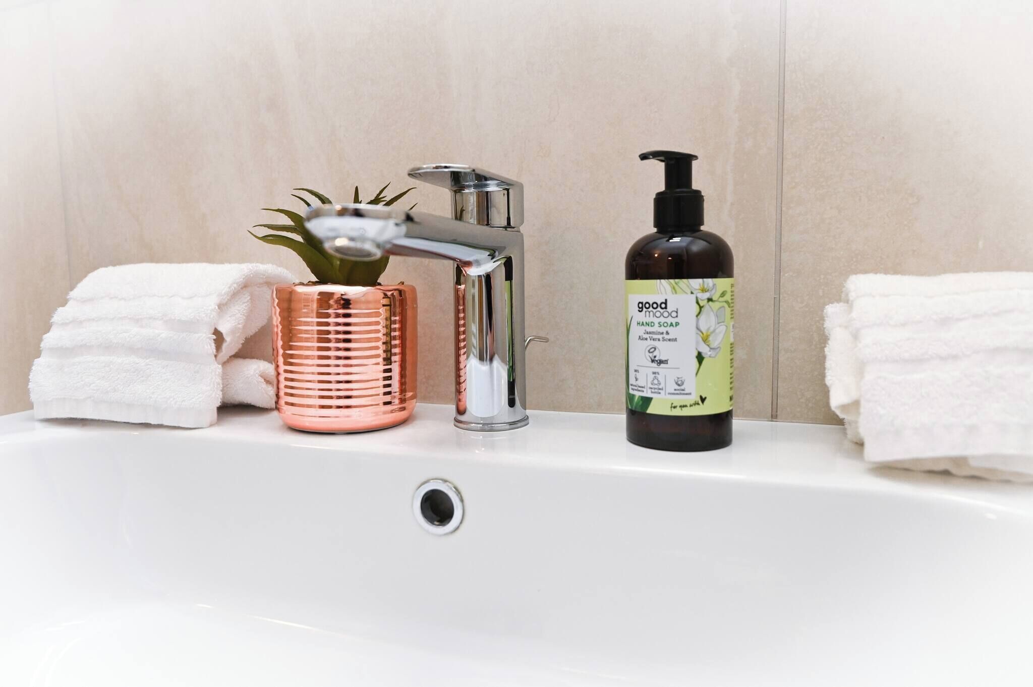 A bathroom sink with a modern faucet, a bottle of hand soap, and a copper-colored container.