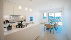 A modern kitchen with a central island, pendant lighting, and a dining area with a view of a coastal landscape. - Serenity Lakefront 2 Bedrooms Retreat in Lugano (Lugano)
