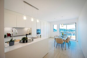 A modern kitchen with a central island, pendant lighting, and a dining area with a view of a coastal landscape. - Serenity Lakefront 2 Bedrooms Retreat in Lugano (Lugano)