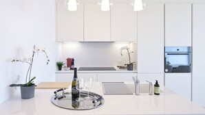 A modern kitchen with white cabinets, pendant lights, a wine bottle, glasses, and a tray. - Serenity Lakefront 2 Bedrooms Retreat in Lugano (Lugano)