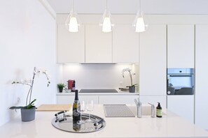 A modern kitchen with white cabinets, pendant lights, a wine bottle, glasses, and a tray. - Serenity Lakefront 2 Bedrooms Retreat in Lugano (Lugano)