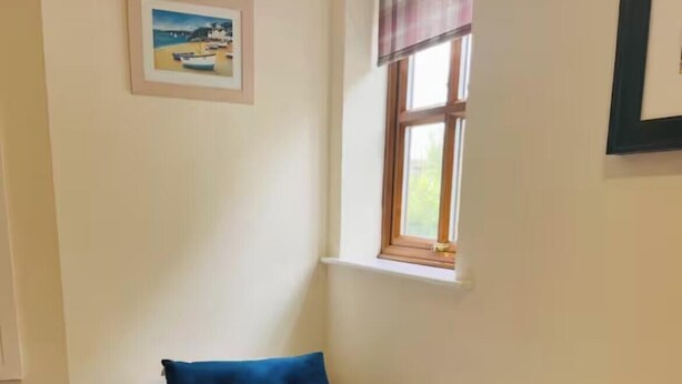 Een kleine kamer met een enkel bed, een raam, een foto aan de muur en een stopcontact.