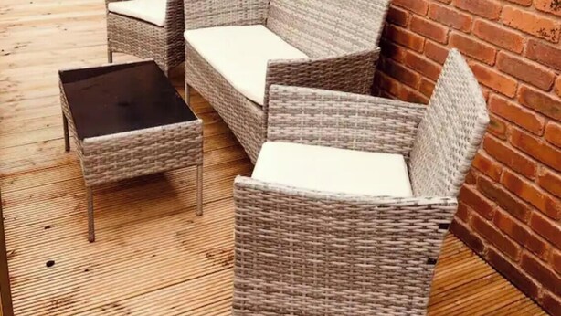 Een rieten zithoek met kussens, een klein tafeltje en een houten terras.