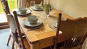 Een houten eettafel gedekt met kommen, borden en wijnglazen, omringd door houten stoelen.