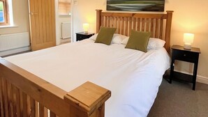 Een slaapkamer met een houten bedframe, wit beddengoed, een schilderij aan de muur en twee bedlampjes.