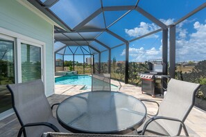 Eine überdachte Terrasse im Freien mit einem Glastisch, zwei Stühlen, einem Grill und einem Swimmingpool.