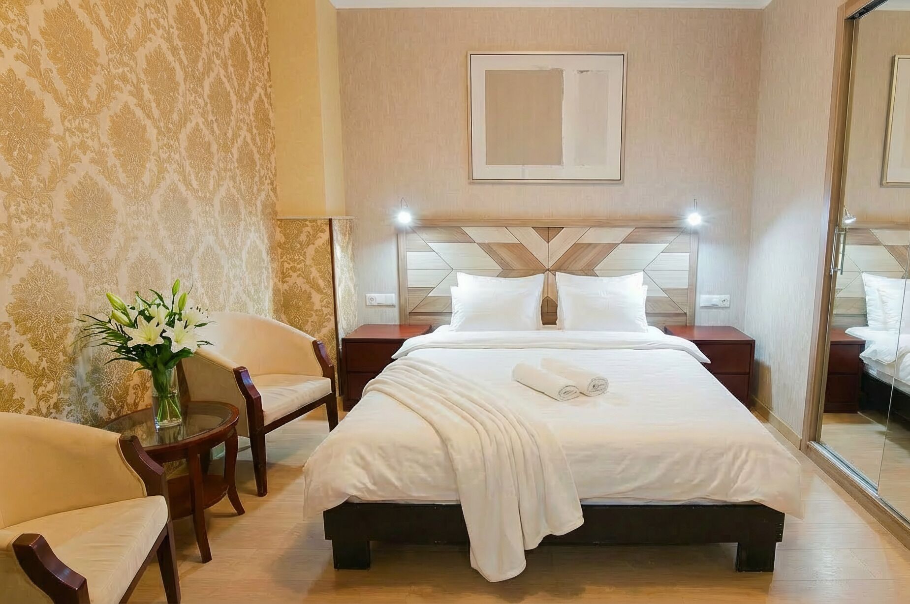 Een hotelkamer met een bed, een stoel, een nachtkastje, een lamp en een spiegel.