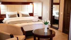 A hotel room with a bed, a chair, a round table, and a vase with flowers.