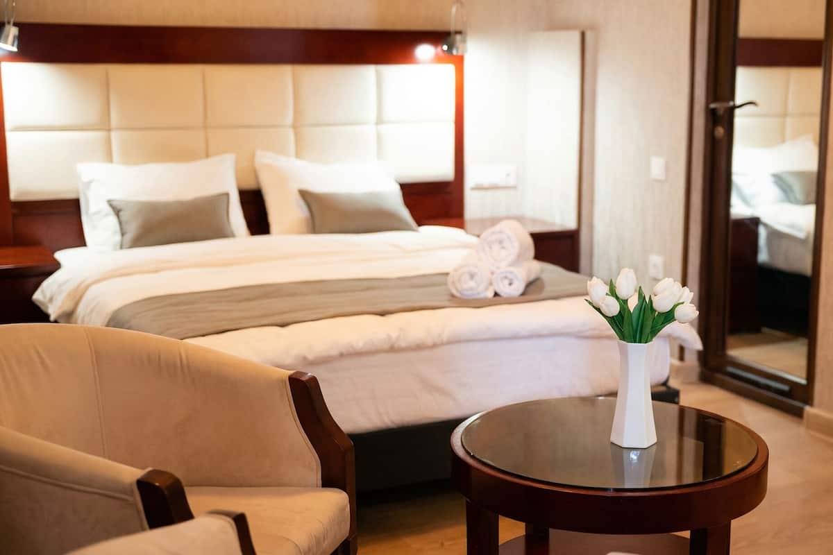 A hotel room with a bed, a chair, a round table, and a vase with flowers.