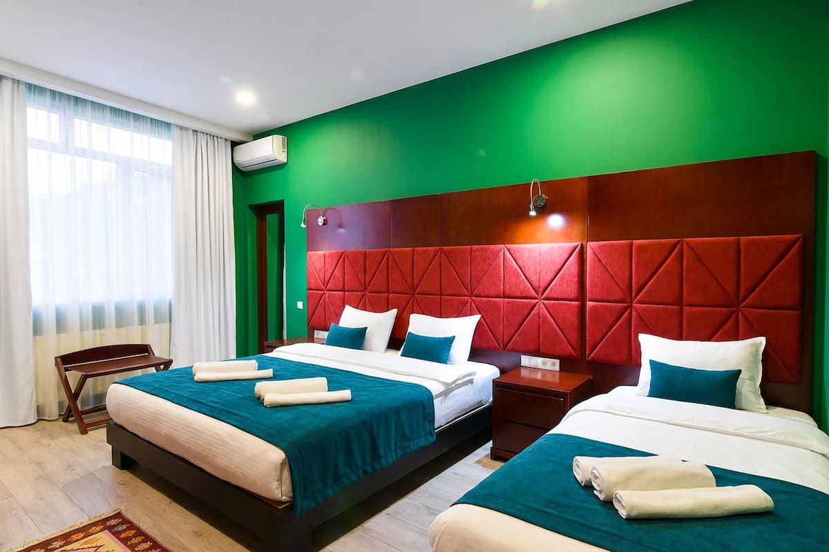 A hotel room with two beds, a red headboard, and a large window with curtains.
