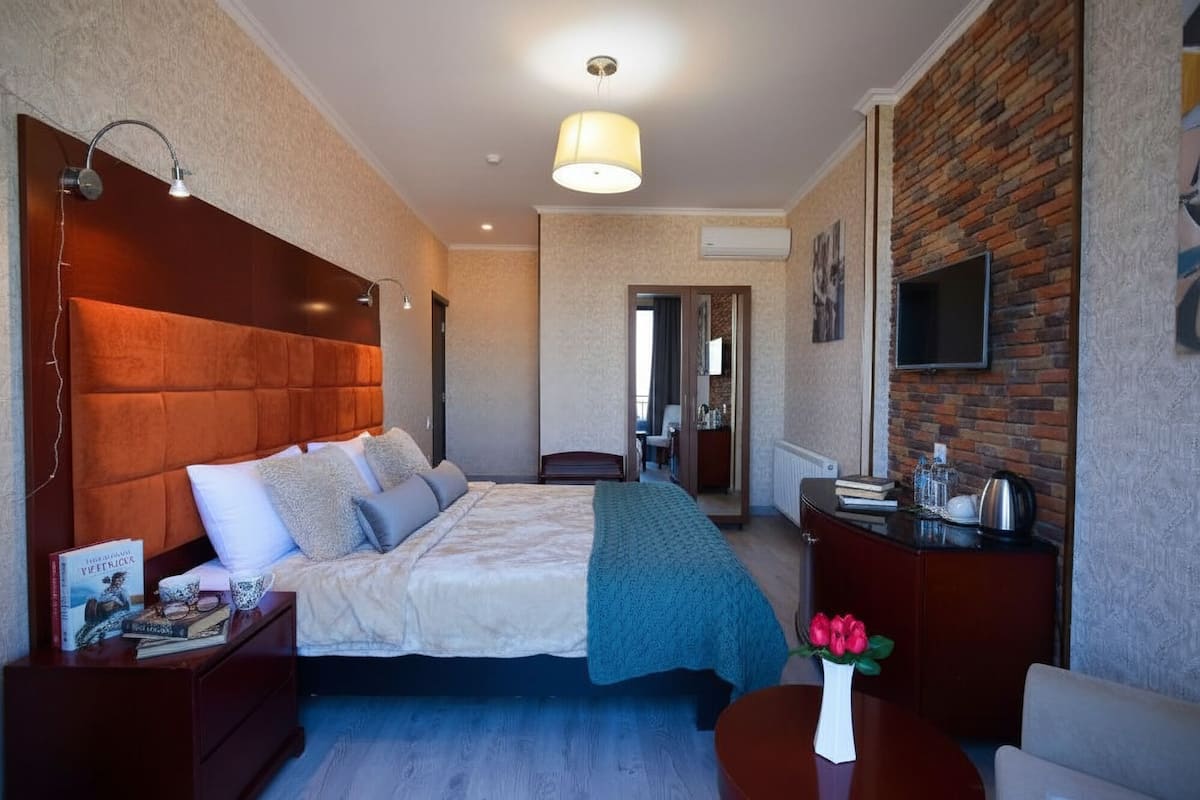 A hotel room with a large bed, a desk with a chair, a TV mounted on the wall, and a brick accent wall.