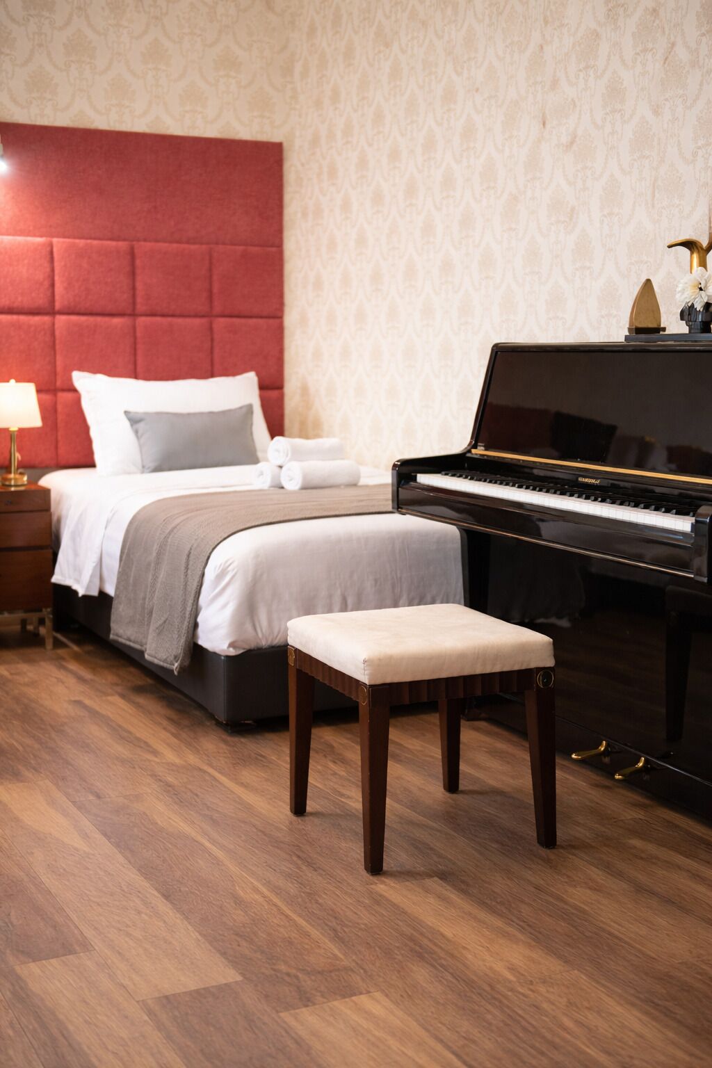 A bedroom with a bed, a bedside table, a lamp, a piano, and a bench.