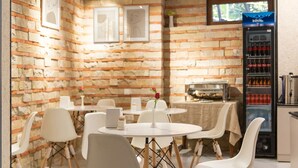 A restaurant with brick walls, white tables, and chairs. There is a coffee machine and a beverage dispenser.