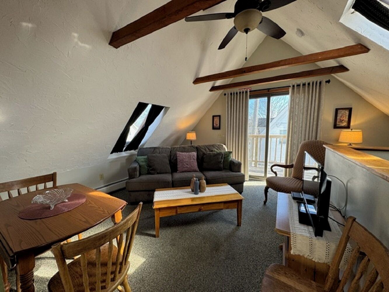 A cozy loft-style living room with a sloped ceiling, a sofa, a coffee table, and a dining table.