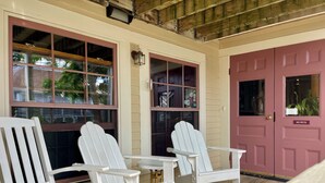 A porch with two white Adirondack chairs, a wooden floor, and a pink door with a 'NO PETS' sign.