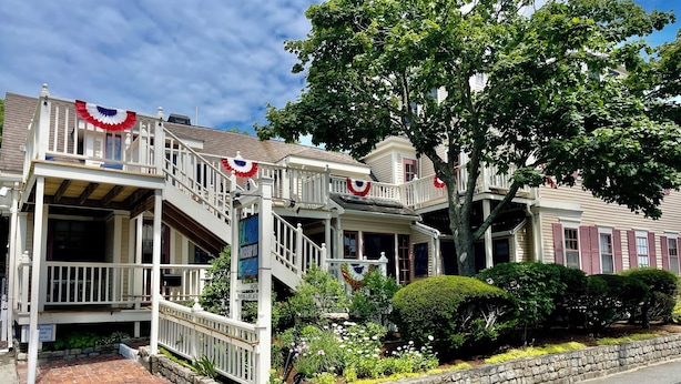 A two-story house with a porch, a staircase, and a stone retaining wall.