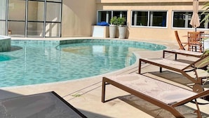 A swimming pool with lounge chairs, a building with multiple balconies, and potted plants. - Apartamento em Cond. de Luxo  (Arraial do Cabo)