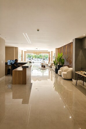 Um lobby moderno com balcão de recepção, área de estar e uma janela grande com vista para carros estacionados.