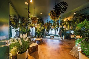 Une pièce spacieuse dotée d’un plancher en bois, de plusieurs coins salon et d’une abondance de plantes d’intérieur.