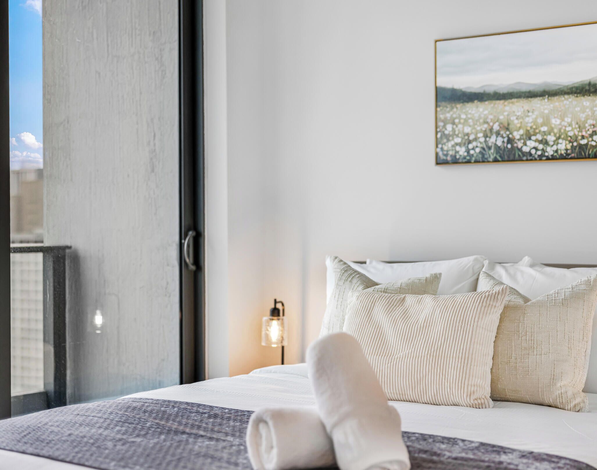 Una habitación de hotel con una cama, una ventana, un cuadro colgado en la pared y una lámpara de noche.