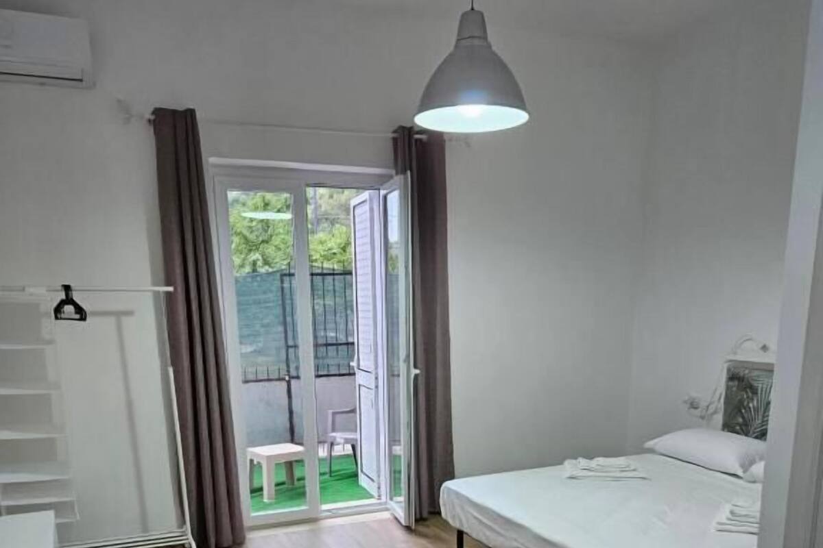 A bedroom with a bed, a desk, and a chair. There is a sliding glass door leading to an outdoor area.