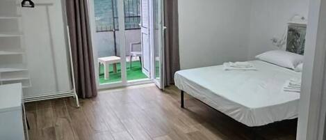 Un dormitorio con una cama, un escritorio y una silla. Hay una puerta corrediza de vidrio que da a un área exterior.