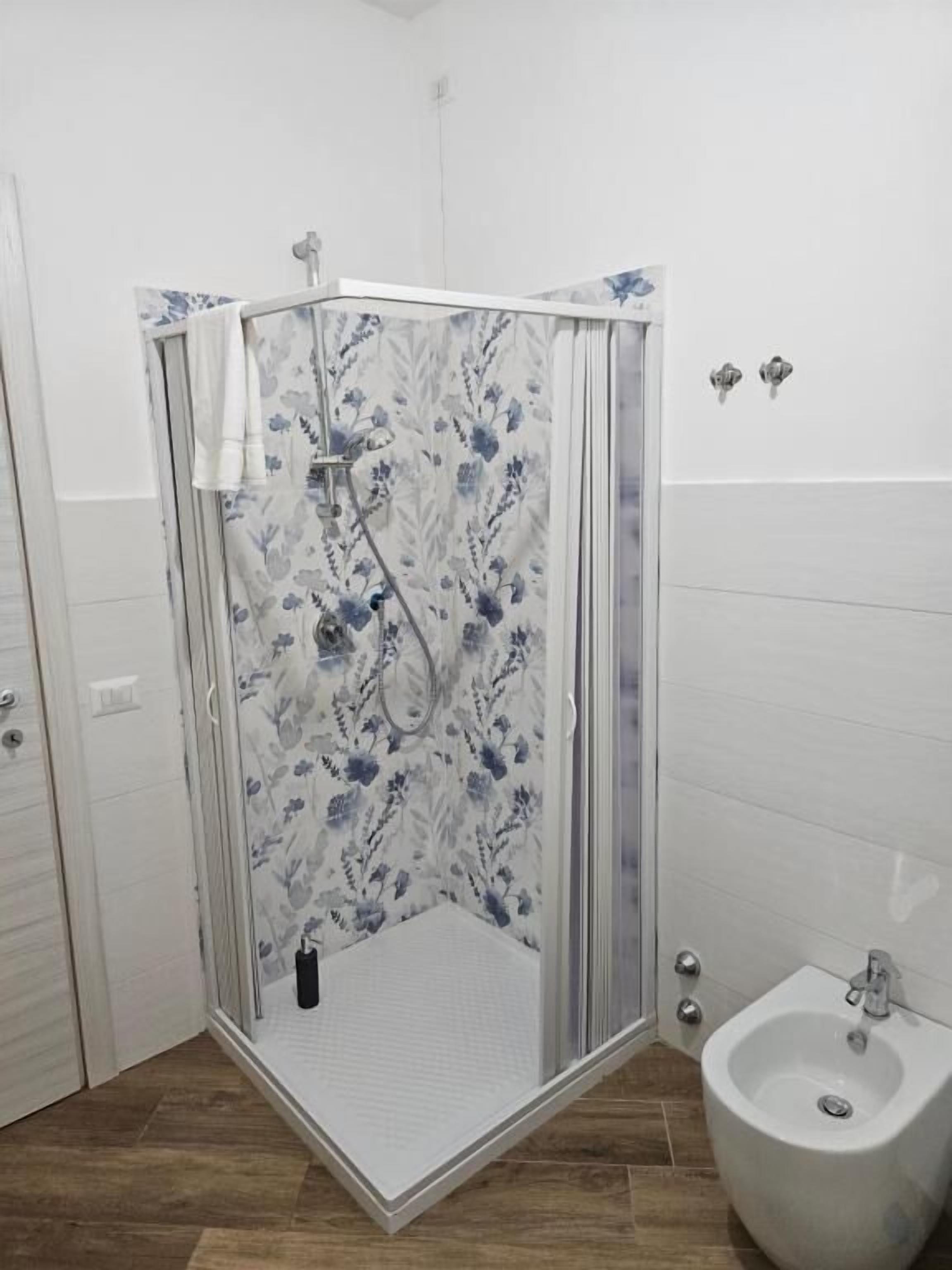 Eine Dusche mit einem blumigen Duschvorhang, einem Bidet und einem Holzboden.