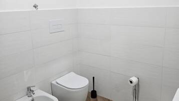 Un baño pequeño y moderno con un bidé, inodoro y un lavamanos reducido.