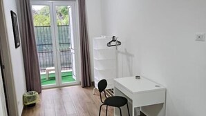 A room with a white desk, a chair, a small white cabinet, a hanging clothes rack, and a sliding glass door leading to an outdoor area. - Onda Blu (Agropoli)