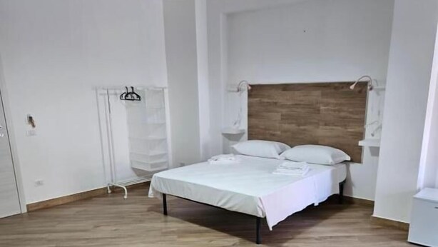 A bedroom with a wooden floor, a bed with white bedding, a hanging light fixture, and a white wardrobe. - Onda Blu (Agropoli)