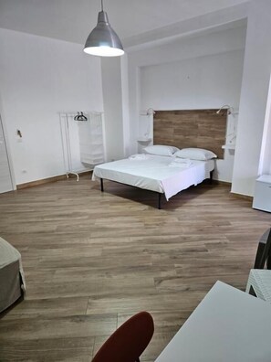 A bedroom with a wooden floor, a bed with white bedding, a hanging light fixture, and a white wardrobe. - Onda Blu (Agropoli)