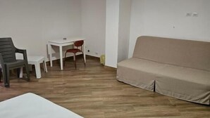 A room with a bed, a sofa, a dining table with chairs, and a hanging light fixture. - Onda Blu (Agropoli)
