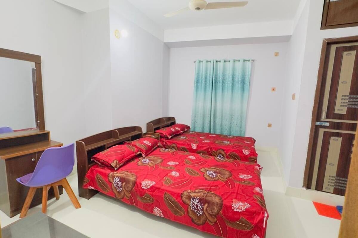 Un dormitorio con cama, escritorio con silla, espejo y ventana con cortinas.