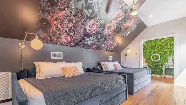 A modern bedroom with two beds, a large floral mural, a ceiling fan, and a green wall.