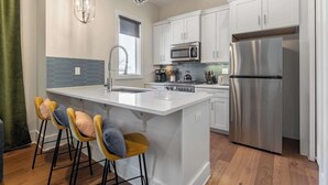 A modern kitchen with white cabinets, stainless steel appliances, a central island with bar stools, and pendant lighting.
