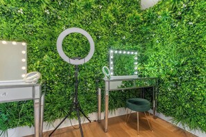 Una habitación con espejo, luz de aro y plantas verdes en la pared.