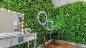 A room with a mirror, ring light, and tripod, surrounded by a green wall.
