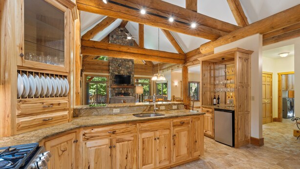 A spacious kitchen with wooden cabinets, a large island with a sink, a built-in stove, and a stone fireplace.