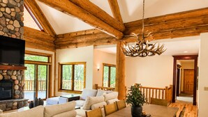 A spacious living area with a fireplace, wooden beams, a dining table, and a view of the outdoors.