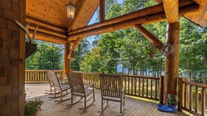 A wooden deck with rocking chairs and a railing, overlooking a forested area.