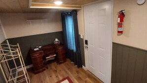 Ein Zimmer mit Holzboden, einer weißen Tür, einem Feuerlöscher, einem Gemälde und einem blauen Vorhang.