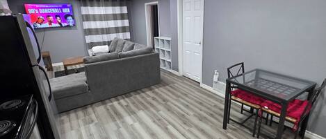 Ein modernes Wohnzimmer mit grauem Sofa, einem Glastisch und einem Flachbildfernseher, der ein Musikvideo zeigt.