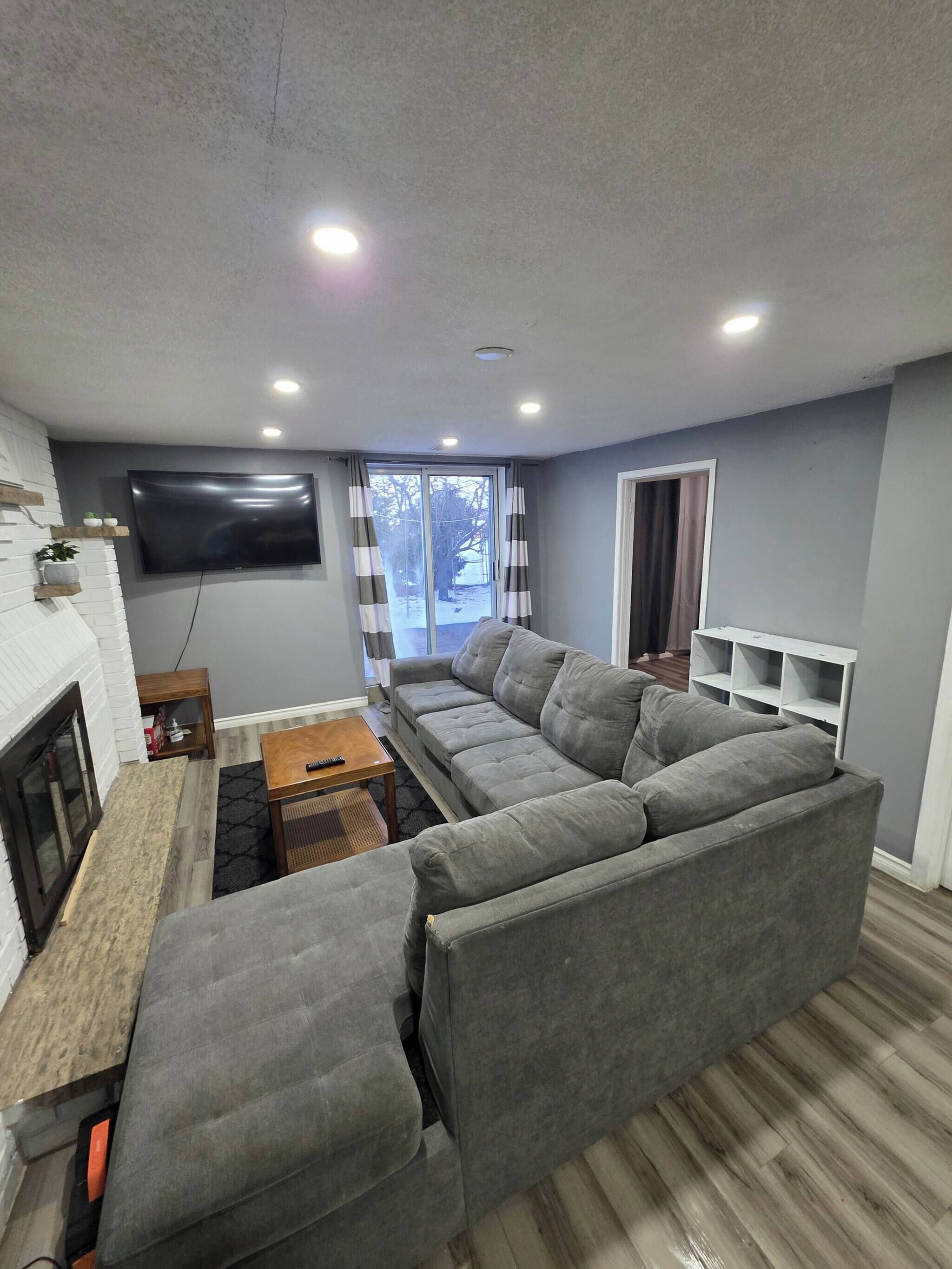 A living room with a grey sofa, a flat-screen TV, a fireplace, and a window with curtains.