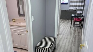 Een gang met een bankje, een badkamer met een wastafel en een woonruimte met een televisie.