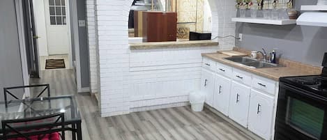 A modern kitchen with white cabinetry, a wooden countertop, and a black stove.