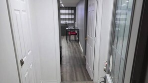 Een gang met een patroonrijk vloerkleed, een eetgedeelte met een tafel en stoelen, en een zicht op een kamer met een gestreept gordijn.