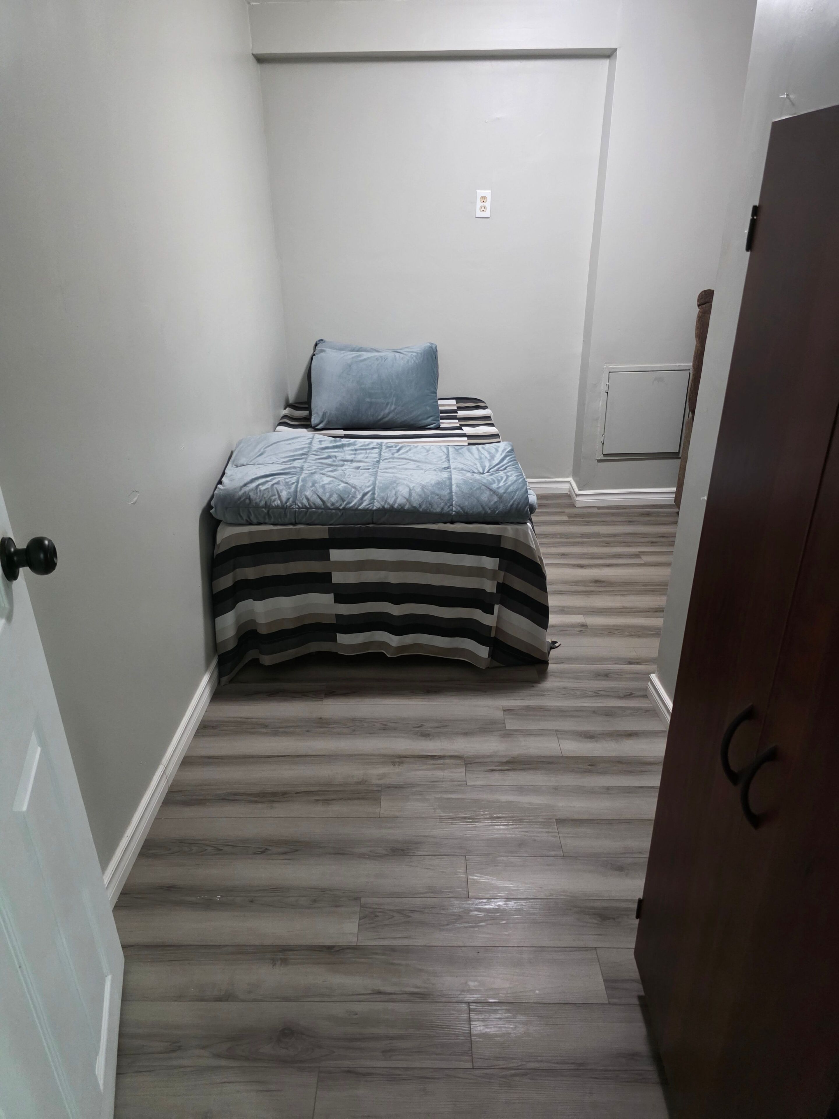 A bedroom with a bed, a door, and a wooden floor.