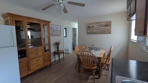 Una cucina con mobili in legno, un tavolo da pranzo con sedie, una ventola a soffitto e un quadro appeso al muro.